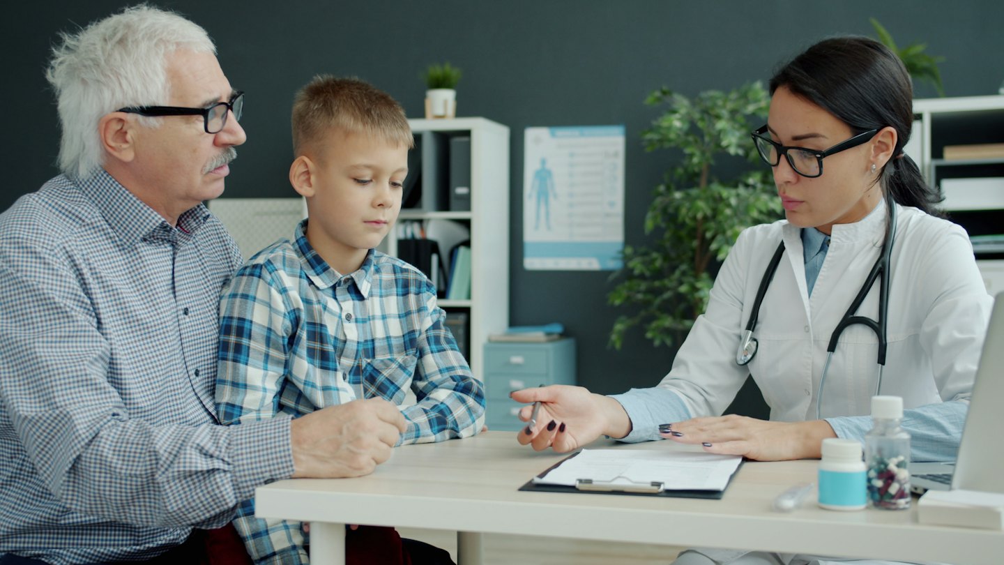 Doctor discusses a document with a man and boy.